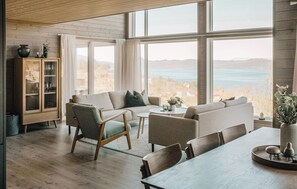 A spacious living room with a large window overlooking a scenic view, a wooden cabinet with glass doors, and a dining area with a table and chairs. - 4 bedroom amazing home in Skånevik (Skånevik)