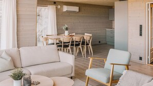 A modern, open-plan living and dining area with wooden walls, a sofa, a dining table with chairs, and a kitchen area with cabinets and an air conditioning unit. - 4 bedroom amazing home in Skånevik (Skånevik)