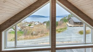 A room with a large window offering a view of a lake, a small house, and a forested area. - 4 bedroom amazing home in Skånevik (Skånevik)