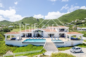 A large, modern villa with a swimming pool, multiple lounge areas, and a view of a lush green hillside. - Villa de 10 Chambres les Pieds Dans L'eau à Guana Bay (Sint Maarten)