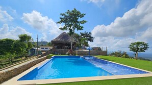 Una piscina rectangular con una estructura de techo de paja al fondo.