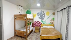 Una habitación con una litera, una cama individual, una mesita de noche pequeña y una pared decorada con motivos vegetales.