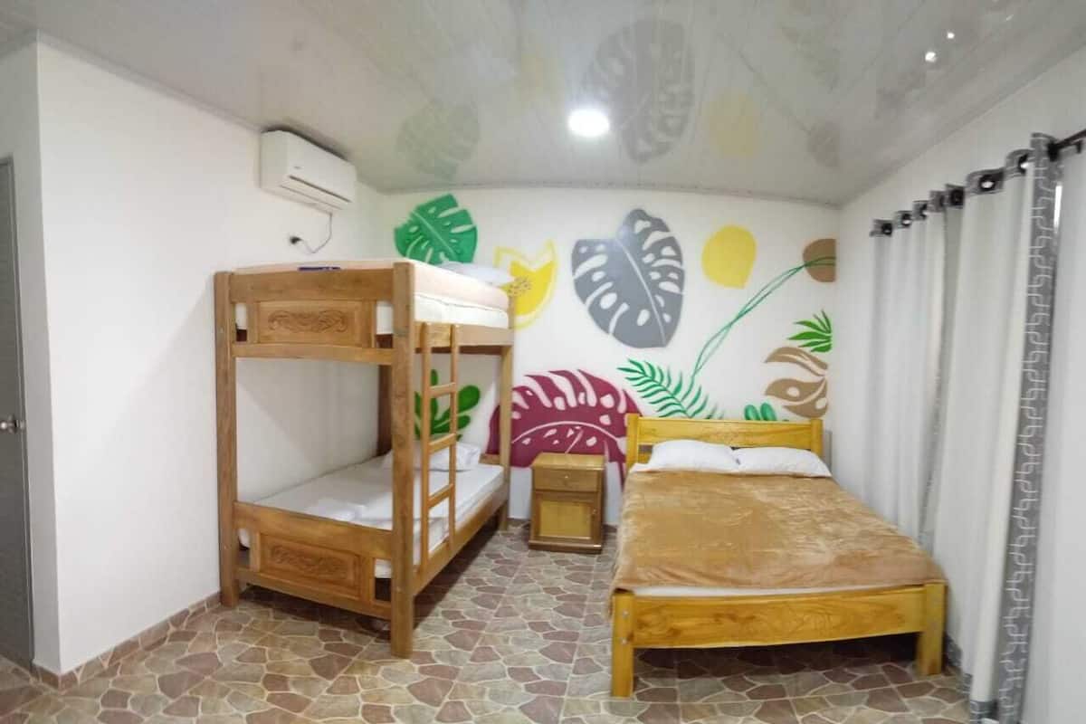 A room with a bunk bed, a single bed, a small bedside table, and a wall decorated with leaf patterns.