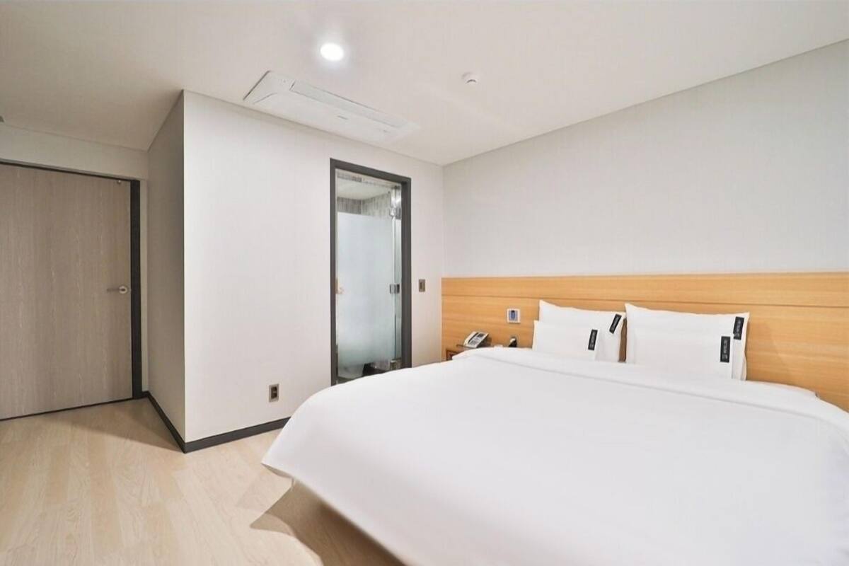 A hotel room with a large bed, a wooden headboard, a bedside phone, and a door with a mirror.