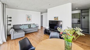 A modern living room with a grey sofa, a flat-screen TV, a wooden dining table, and a vase of flowers. - Lovely apartment in Tettnang with WiFi (Tettnang)
