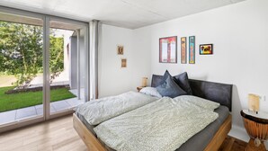 A modern bedroom with a large bed, a sliding glass door leading to a garden, and several framed artworks on the wall. - Lovely apartment in Tettnang with WiFi (Tettnang)
