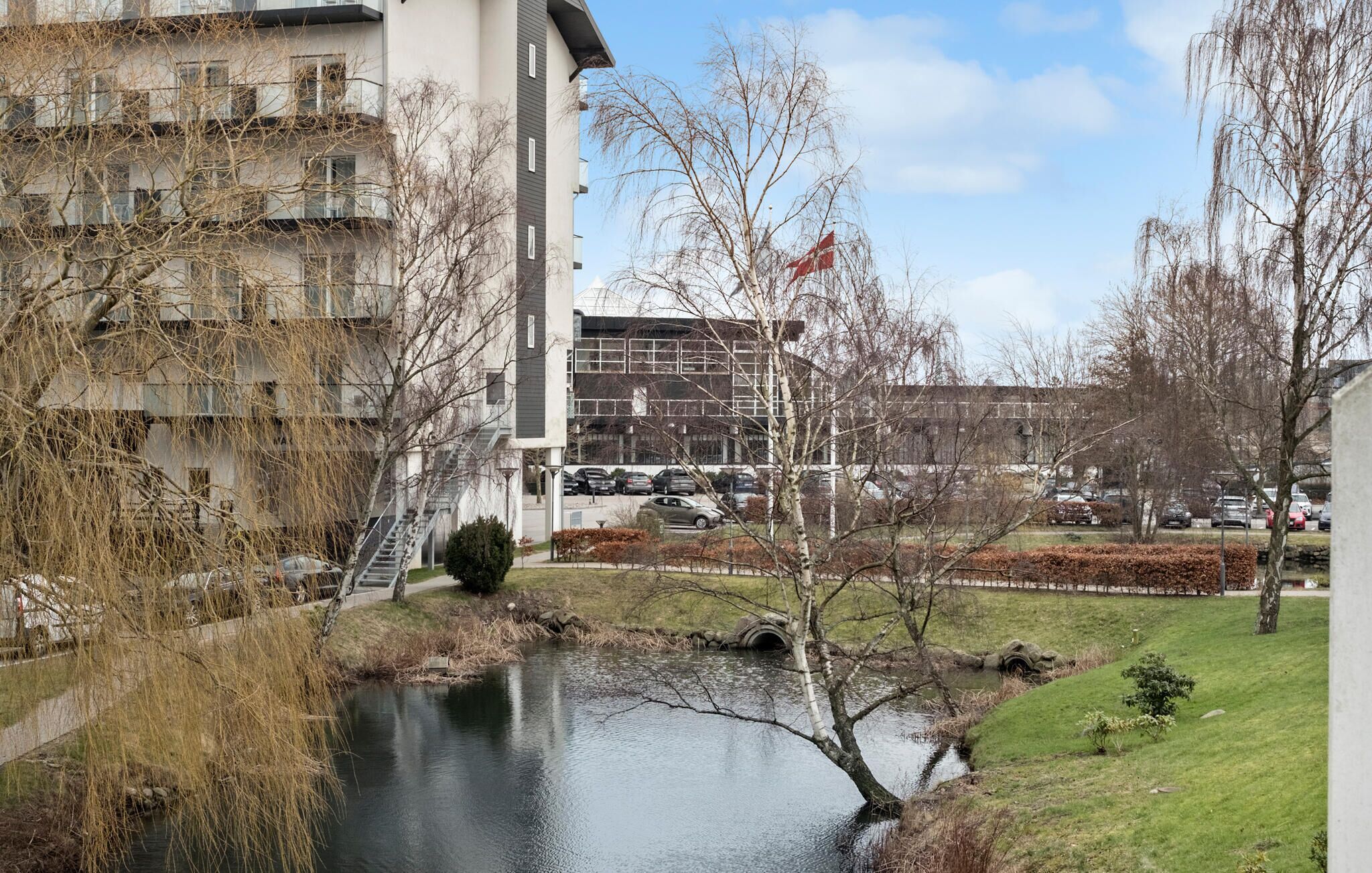 A riverside view with a modern building, a parking lot, and a flag on a flagpole.