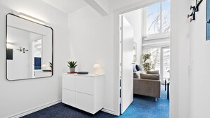 Un couloir moderne et bien éclairé, avec une armoire blanche, un miroir et un sol à motifs à pois bleus.