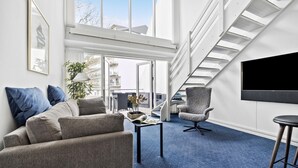Un salon moderne avec un canapé, un fauteuil et un téléviseur fixé au mur.