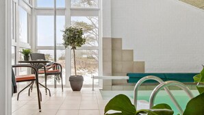 A sunlit room with a large window, a seating area with a bench, and a small table with chairs. - Nice home in Bindslev with sauna (Bindslev)