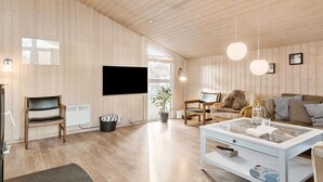 A spacious living room with wooden walls, a flat-screen TV, a glass coffee table, and a comfortable seating area. - Nice home in Bindslev with sauna (Bindslev)