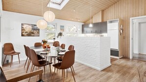 A modern kitchen with white brick accents, a dining area with a round table and brown chairs, and a large window providing natural light. - Nice home in Bindslev with sauna (Bindslev)