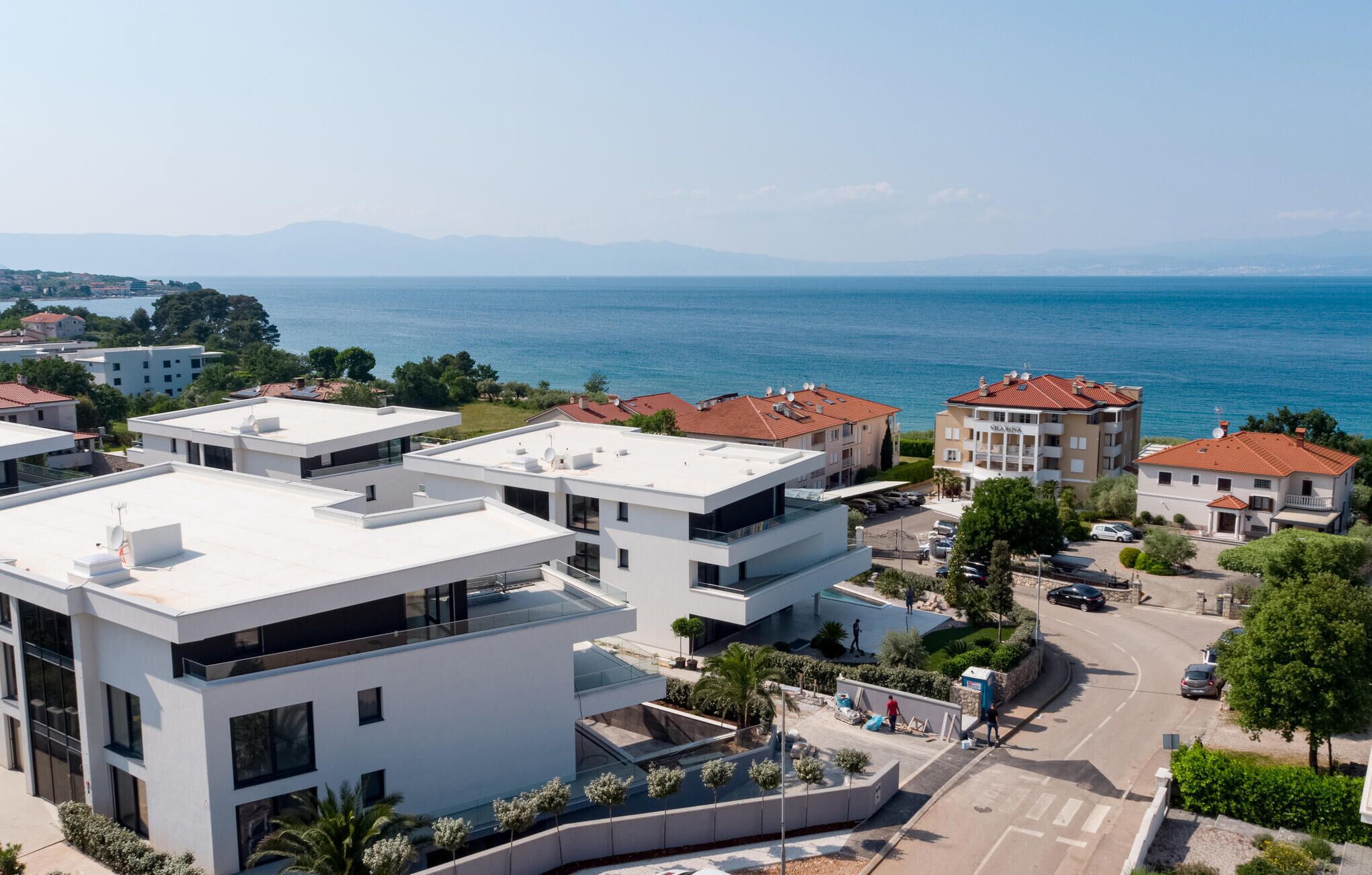 Una zona residencial moderna con edificios blancos, vista al mar y cielo despejado.