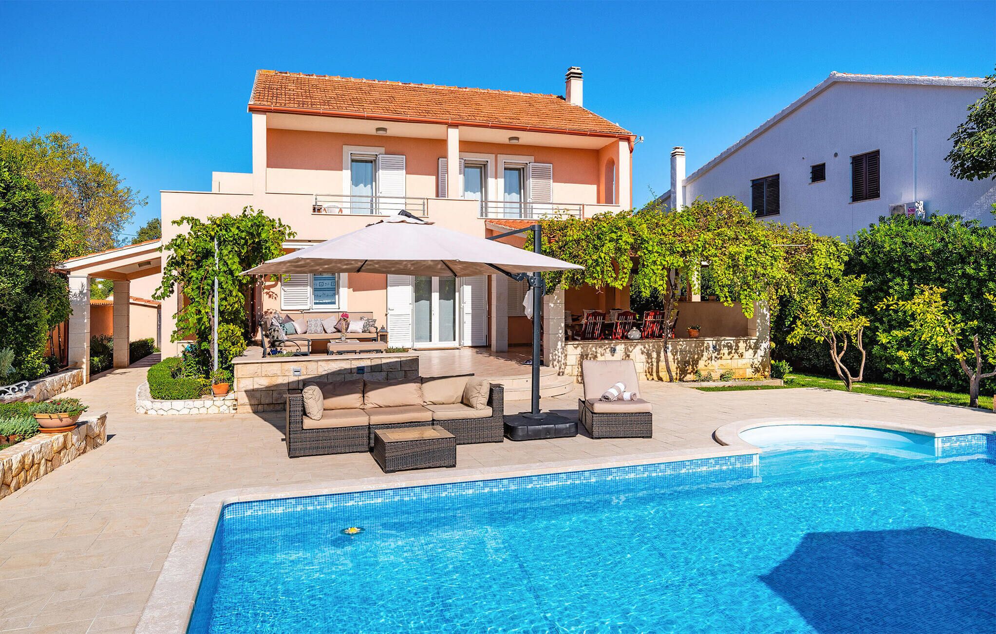 Ein zweistöckiges Haus mit Schwimmbad, Gartenmöbeln und einer überdachten Terrasse.