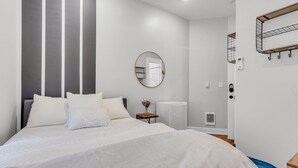 Une chambre d’hôtel moderne avec un grand lit, un miroir rond, une petite table avec un vase et une table de chevet en bois.