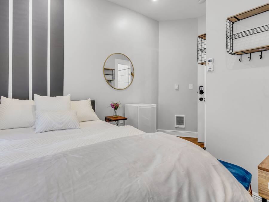 A modern hotel room with a large bed, a round mirror, a small table with a vase, and a wooden side table.