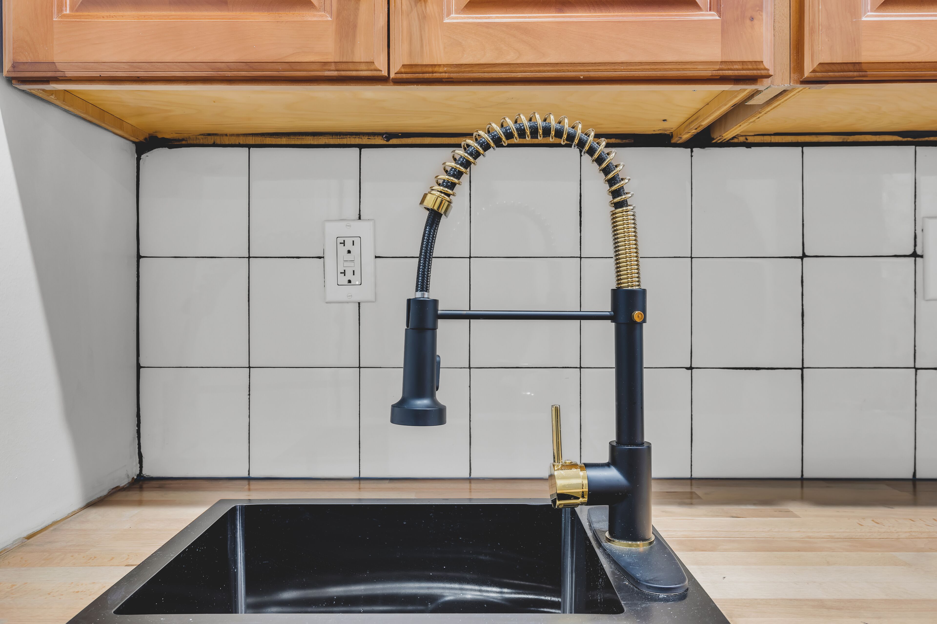 A kitchen with a black sink, a faucet with a flexible hose, and wooden cabinets above.