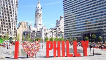 A city square with a prominent 'I ♥ PHILLY' sign, a historic building, and modern skyscrapers in the background.