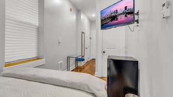 A modern hotel room with a bed, a TV mounted on the wall, a small table, and a door leading to another room.