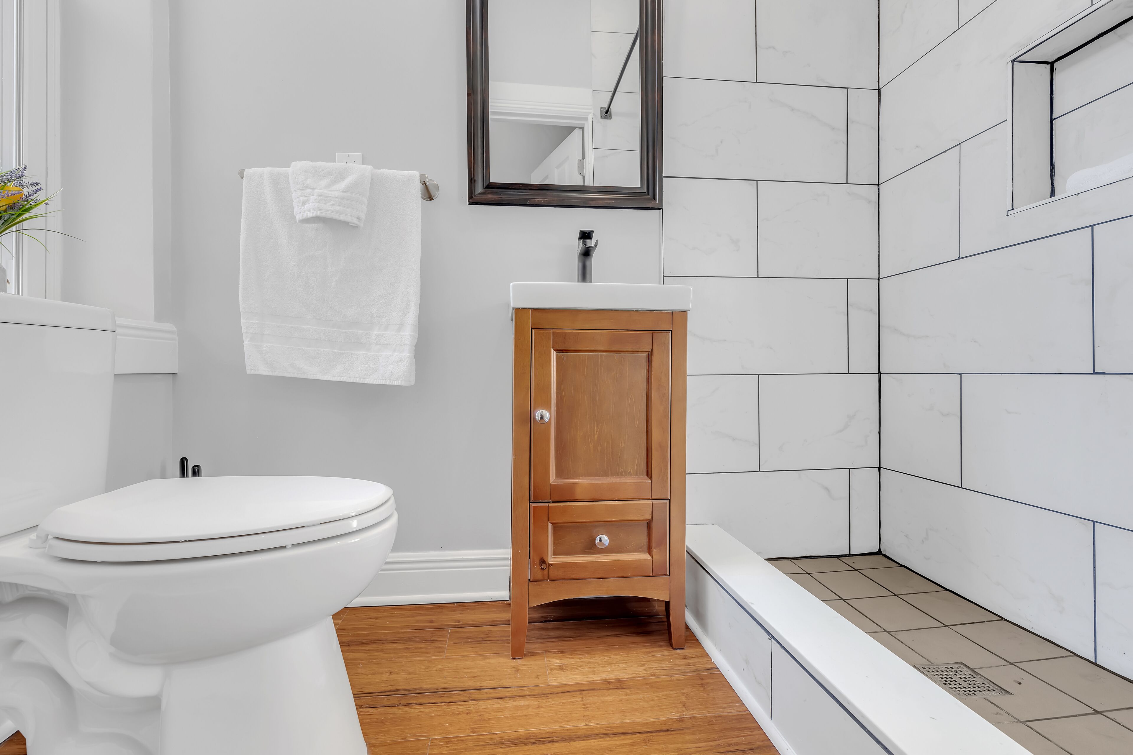 Un baño moderno con inodoro blanco, tocador de madera y bañera.