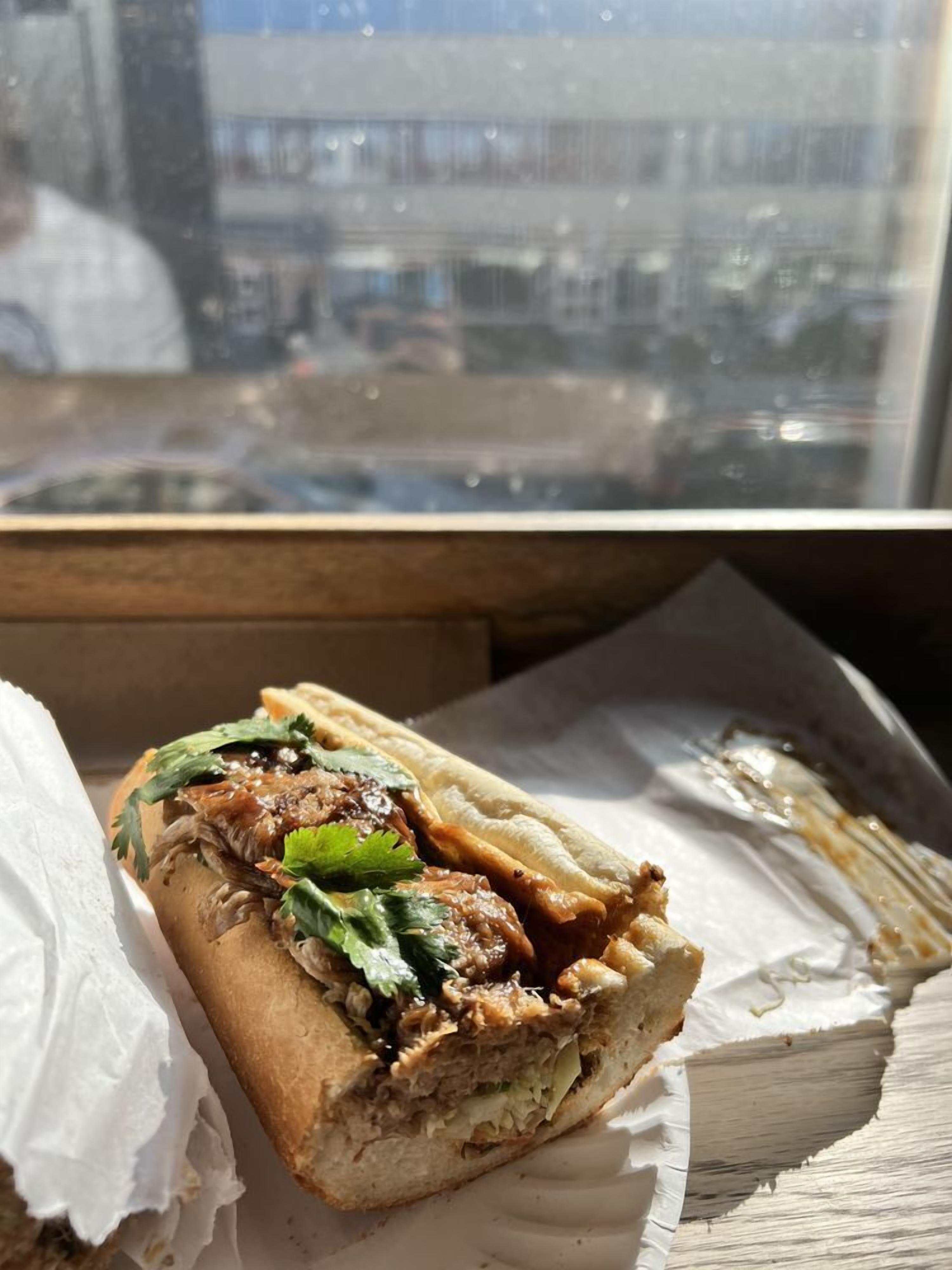A sandwich on a paper plate with a window view in the background.