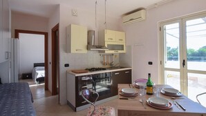 Cocina compacta con estufa, horno y utensilios colgando. Se ha dispuesto una mesa de comedor con platos y una botella.