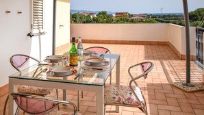Una mesa de vidrio con sillas en un balcón, una botella de vino Borsalino y vistas a casas y vegetación.