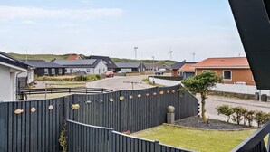 A residential area with houses, a fenced yard, and wind turbines in the background.