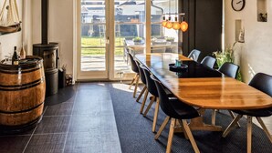 A modern dining area with a long wooden table, black chairs, and a rustic barrel.