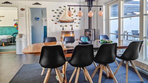 A dining area with a wooden table, black chairs, and a view of the sea through large windows.