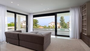 Een moderne slaapkamer met een groot bed, schuiframen naar een balkon en uitzicht op zee en gebouwen.
