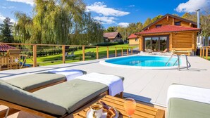 Een houten chalet met een zwembad, ligstoelen en een tafel met ontbijtartikelen.