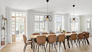 Une salle à manger avec une grande table en bois, des chaises marron et des luminaires suspendus.