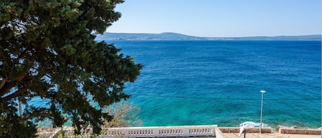 A coastal view with a clear blue sea, a white railing, and a bench.