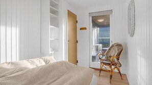 A bedroom with a bed, a chair, and a door leading to a balcony.