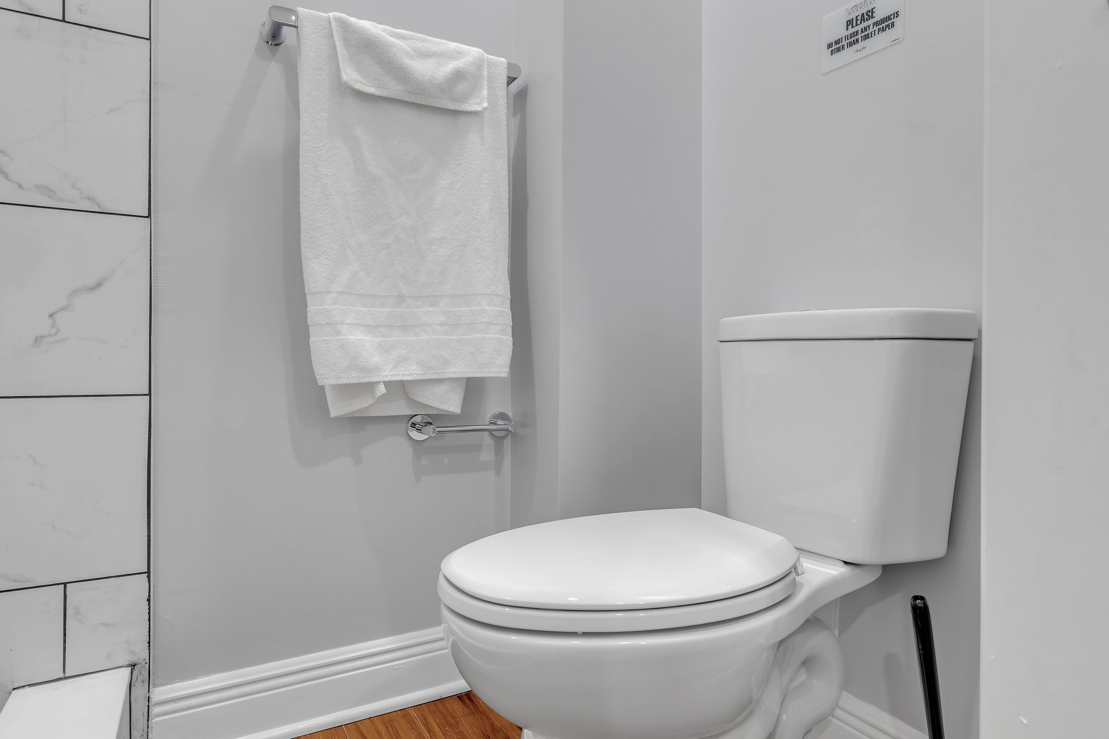 A white toilet with a white tank, a towel hanging on a metal rack, and a sign on the wall.