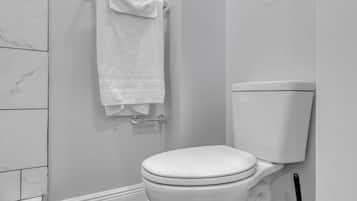 A white toilet with a white tank, a towel hanging on a metal rack, and a sign on the wall.