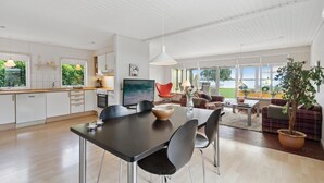 A modern kitchen with white cabinets, a dining area with a black table and chairs, and a living room with a sofa and a potted plant. - Amazing home in Sunds with lake view (Sunds)