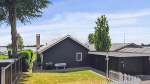 A dark wooden building with a sloped roof, a bench, and a white picket fence in a grassy yard. - Amazing home in Sunds with lake view (Sunds)