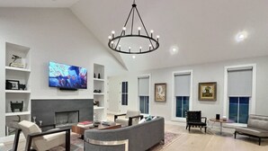 A modern living room with a fireplace, a large TV, and a chandelier.