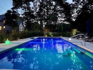 A rectangular swimming pool with a blue tint, surrounded by a wooden deck and a metal railing.