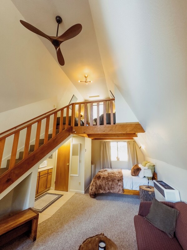 A spacious loft bedroom with a wooden staircase, a large bed, and a cozy seating area.