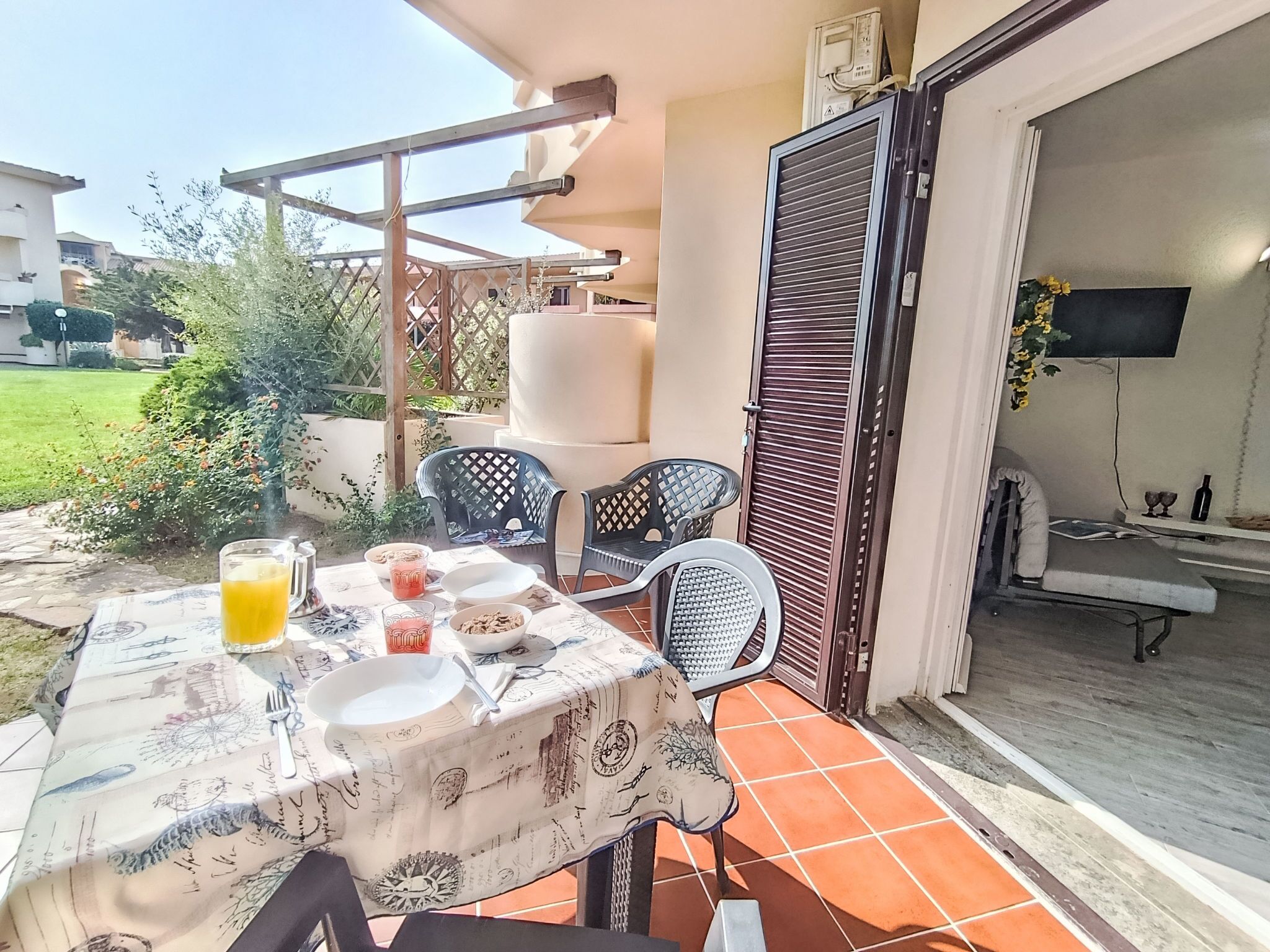 An outdoor patio with a table set for dining, surrounded by chairs, and a TV mounted on the wall.