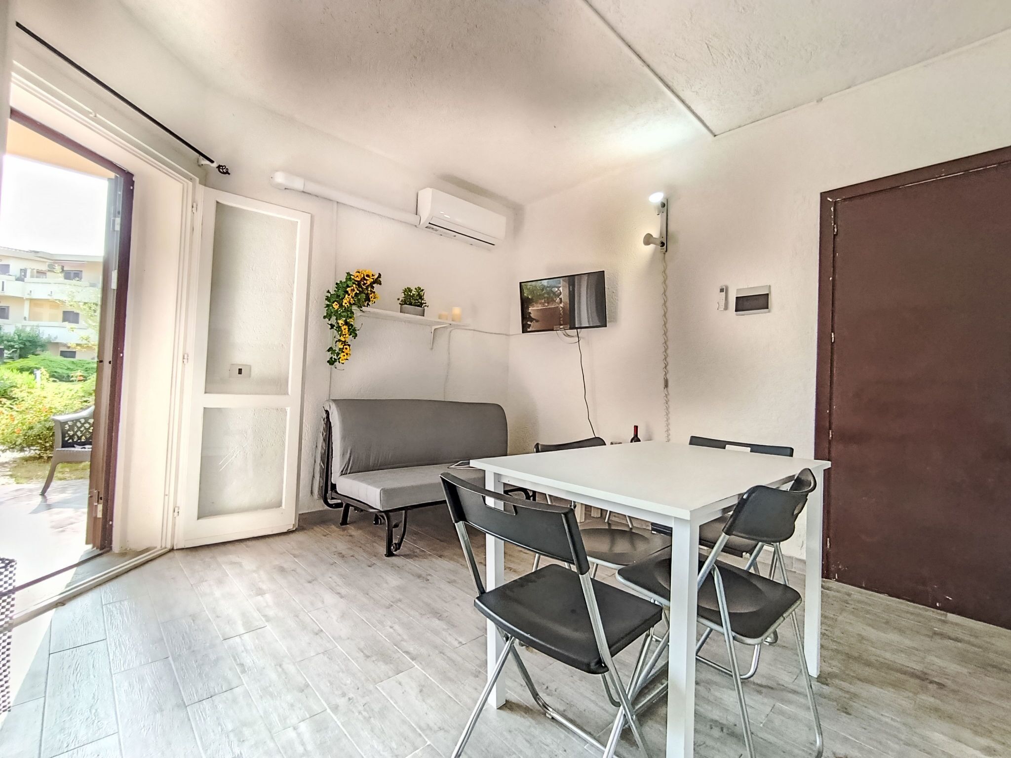 A modern room with a white table, black chairs, a grey sofa, and a TV mounted on the wall.