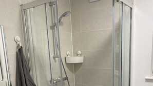 Une salle de bain moderne avec une douche à parois de verre, des toilettes blanches et un meuble-lavabo doté d’un miroir et d’un porte-serviettes.