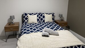 Un lit bien fait, avec une couvre-lit à motifs, deux lampes de chevet et une serviette pliée posée sur le lit.