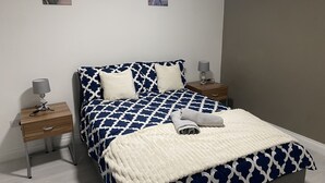 Un lit bien fait, recouvert d’une couvre-lit à motifs, deux tables de chevet avec des lampes et deux tableaux accrochés au mur.