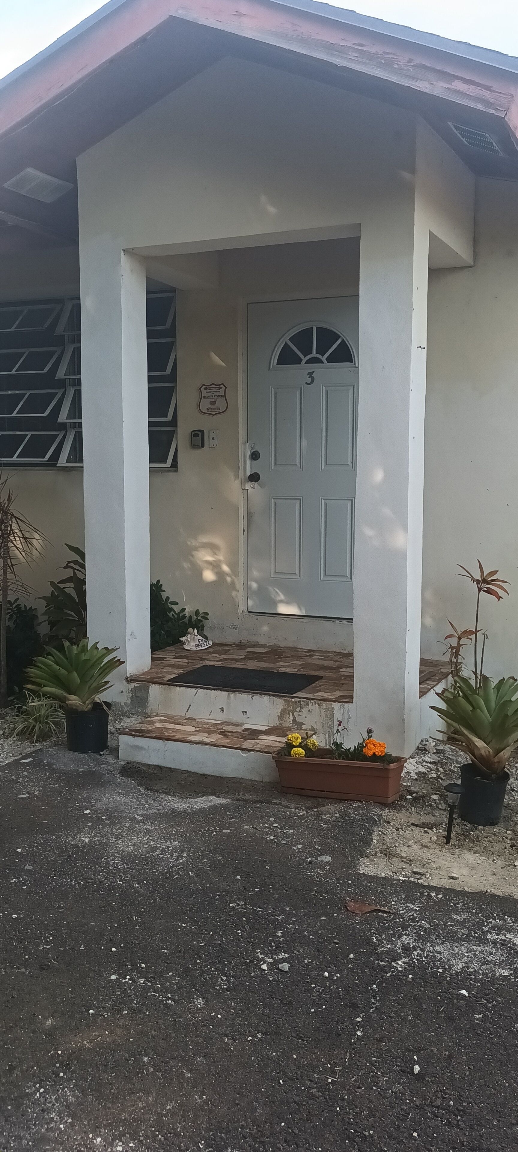 A building with a white exterior, a door marked with the number 3, and a small porch area with potted plants.