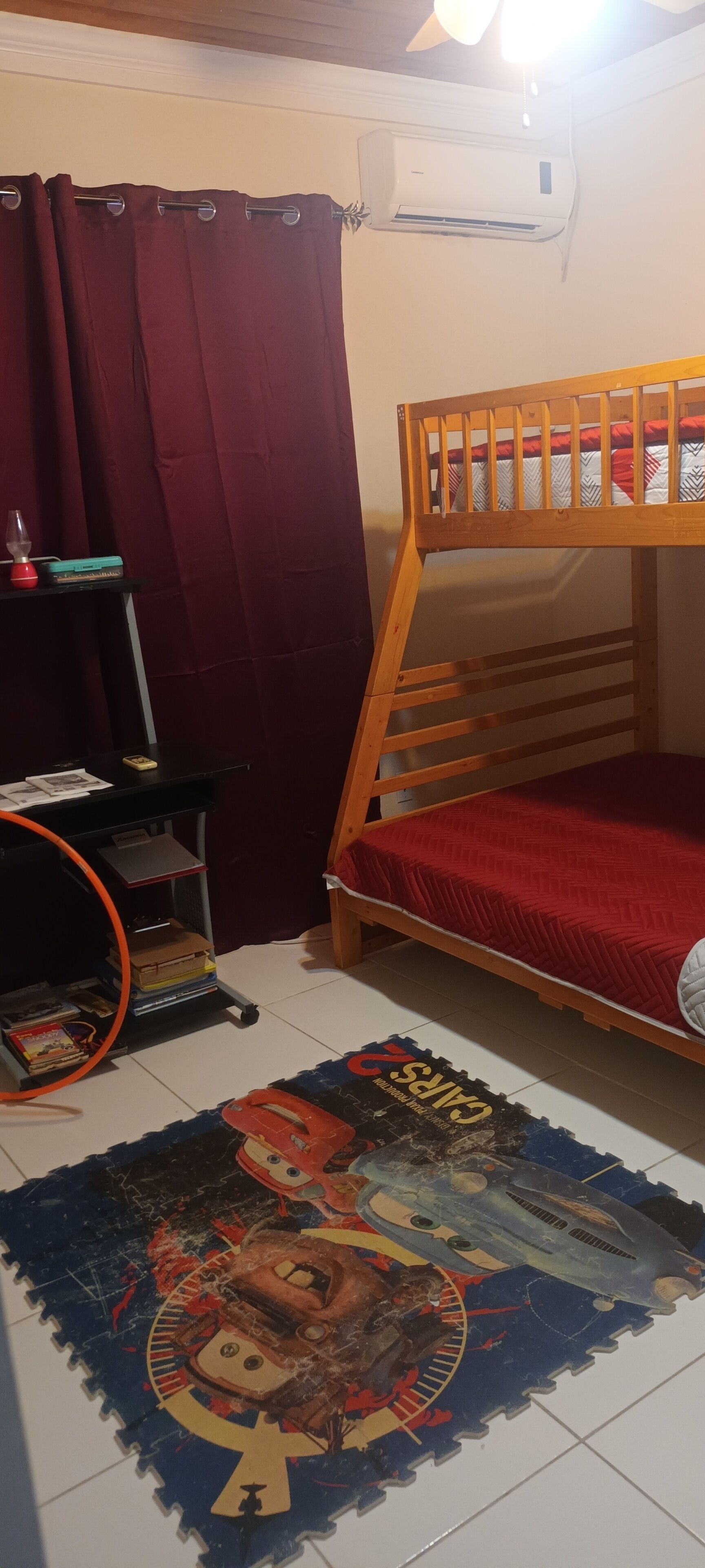 Un lit superposé avec un matelas rouge, un bureau avec une lampe à lave et une lampe à lave posée sur une étagère.