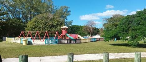 A playground with swings, a slide, and a small pavilion.